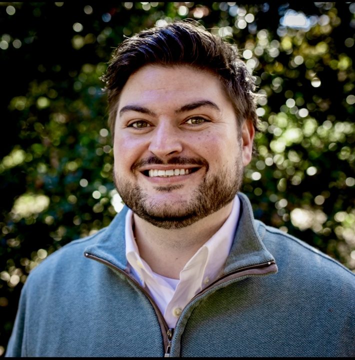 Portrait of Michael Morgan smiling, wearing a blue quarter-zip over a white collared shirt